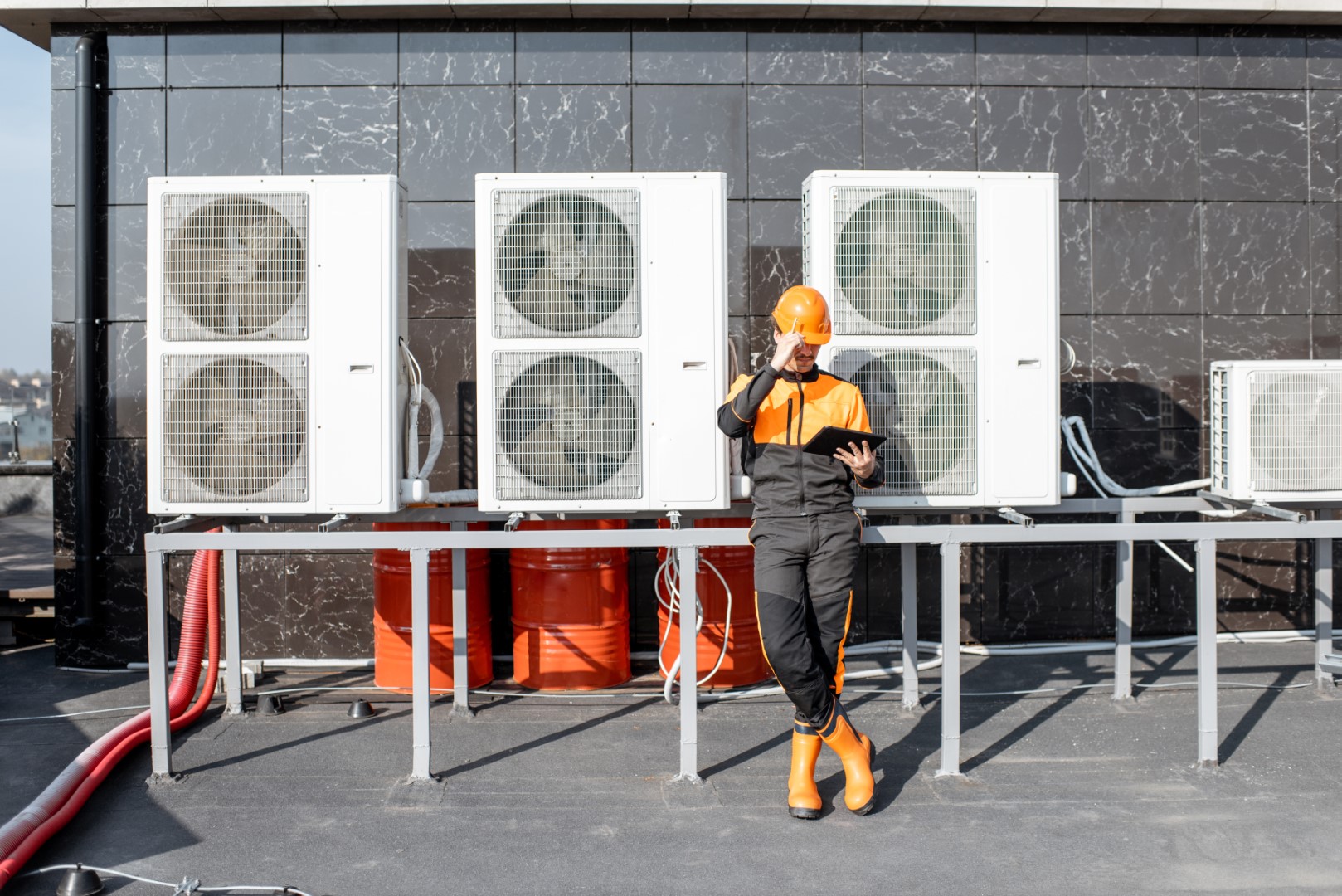 Egineer in protective workwear designing with digital tablet, while standing near the outdoor units of the air conditioner or heat pump